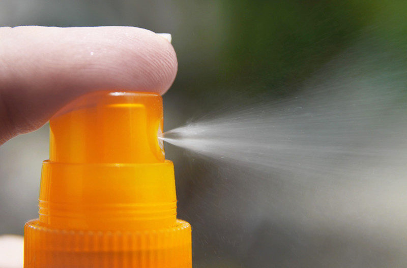 An orange spray bottle pushed by a finger